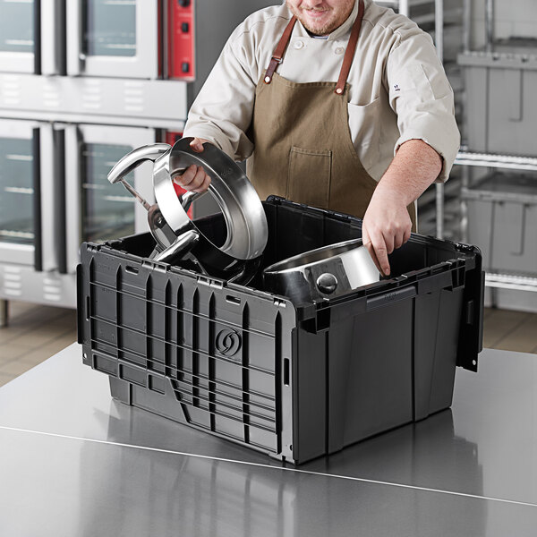 A man in an apron putting a pot and pan into a black Orbis tote box.