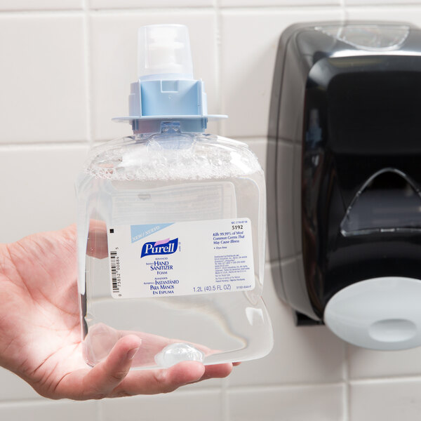 A hand holding a bottle of Purell FMX Advanced foaming hand sanitizer.
