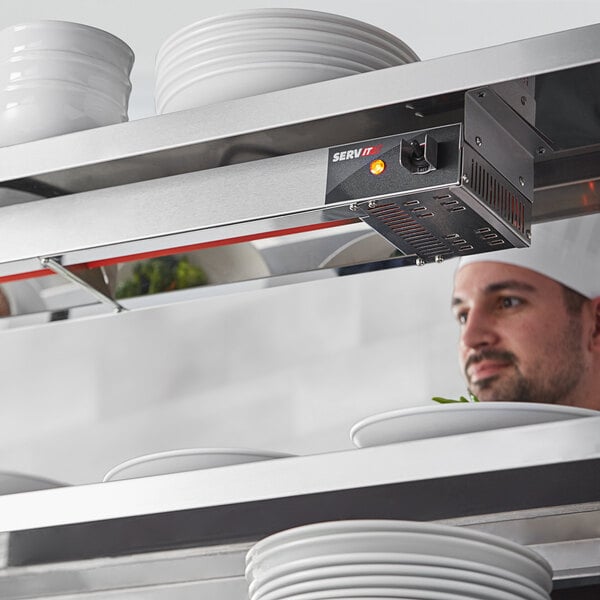 A chef in a white chef's hat using a ServIt high wattage strip warmer to heat plates.