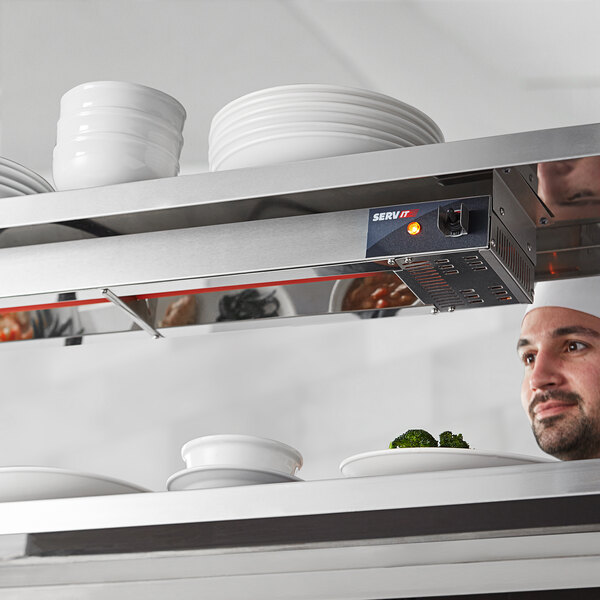 A man in a professional kitchen using a ServIt strip warmer on a shelf with plates.