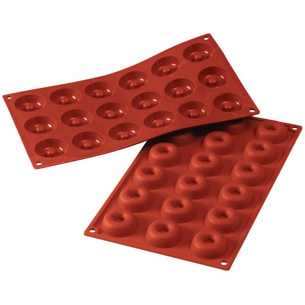 A couple of red Silikomart silicone baking molds with small holes in each cavity.