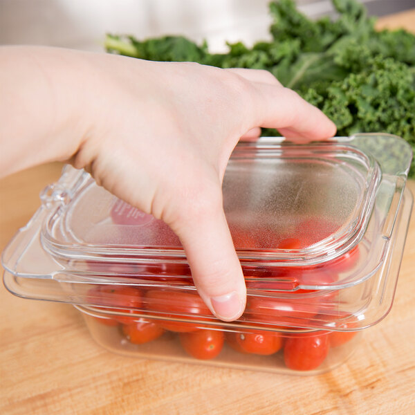 A hand reaching out to a Carlisle plastic container with tomatoes.