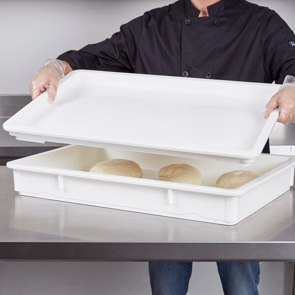 A chef using a Cambro white pizza dough proofing box lid to hold a tray of pizza dough.