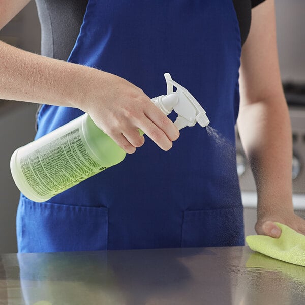 A person in a blue apron using a Bacoff spray bottle to disinfect a professional kitchen counter.