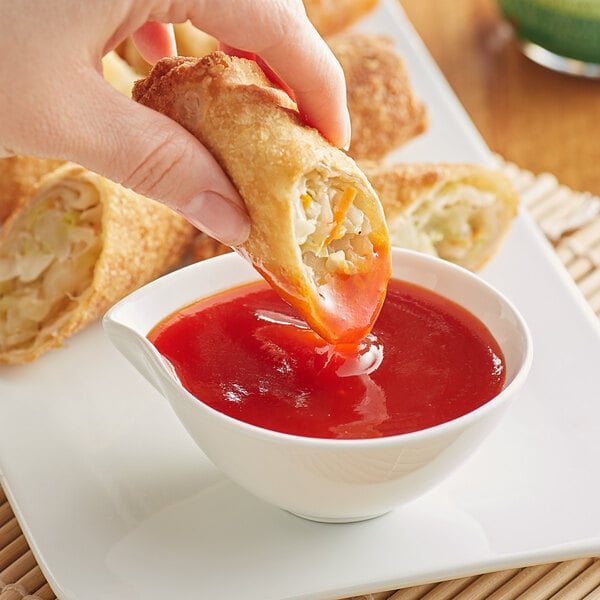 A hand dipping a vegetable egg roll into a bowl of Lee Kum Kee sweet and sour sauce.