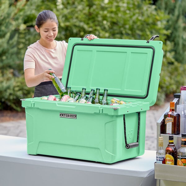 A woman putting green bottles into a seafoam green CaterGator outdoor cooler.
