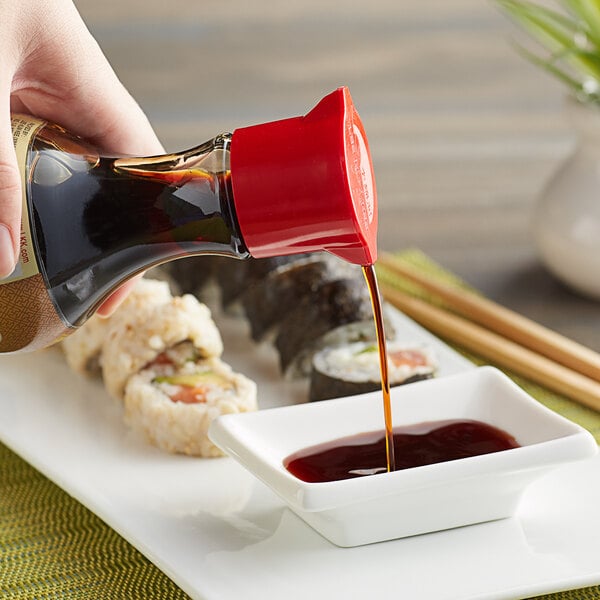 A hand pouring Lee Kum Kee soy sauce onto a bowl of sushi.
