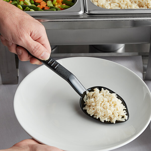 A person using a Carlisle black high heat salad bar spoon to serve rice.