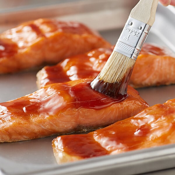 A person using a paint brush to apply Lee Kum Kee Teriyaki Glaze to salmon.