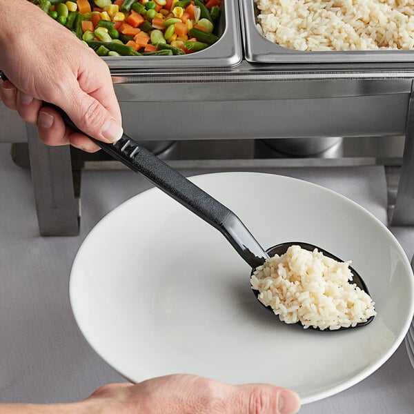 A hand holding a black Carlisle salad bar spoon over a plate of rice.
