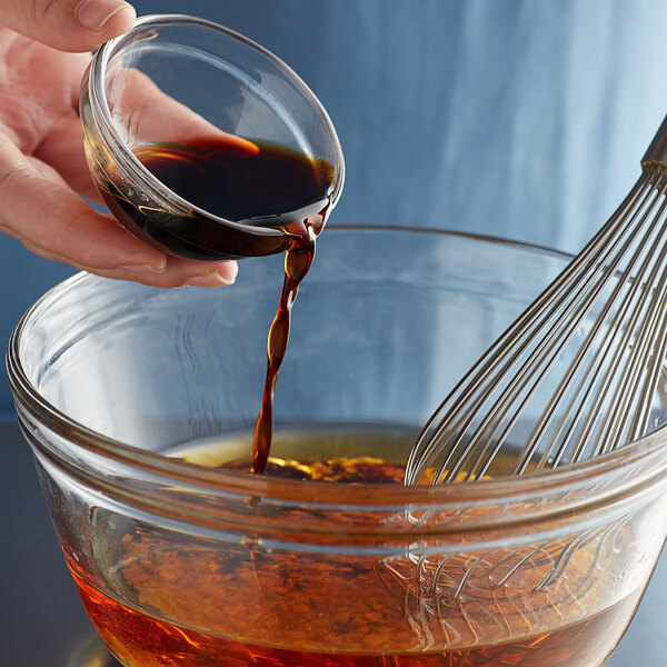 A hand pouring Lee Kum Kee less sodium soy sauce into a glass bowl.