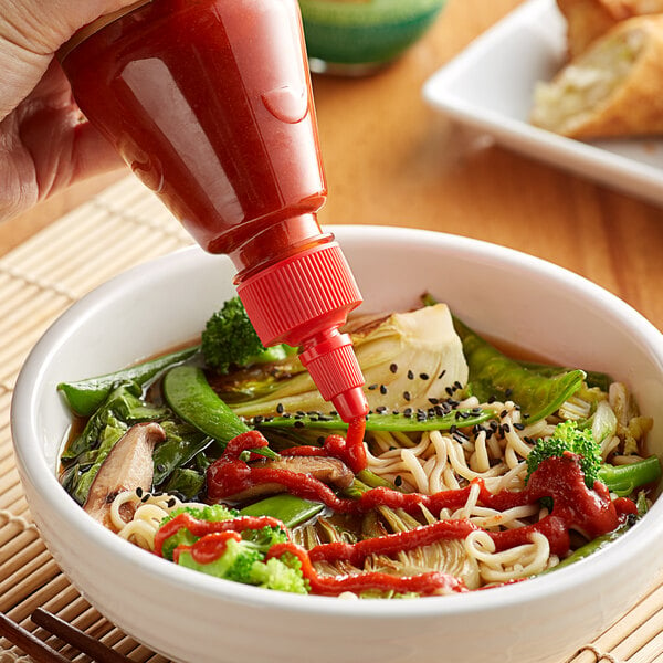 A person pouring Lee Kum Kee Sriracha Chili Sauce on a bowl of noodles.