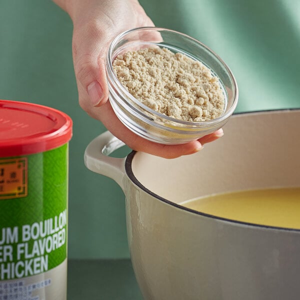 A hand pouring Lee Kum Kee Premium Chicken Flavored Bouillon Powder into a pot.