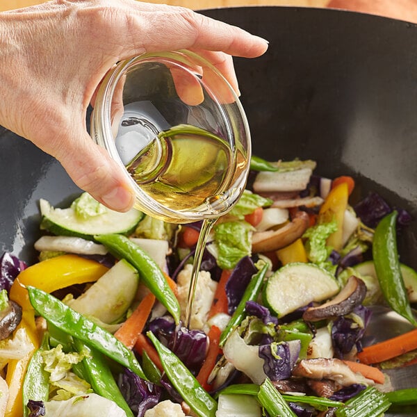 A hand pouring Lee Kum Kee Kum Chun Sesame Flavored Seasoning Oil into a bowl of salad.