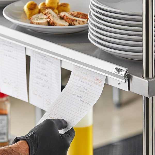 A hand placing a receipt on a wall-mounted ticket holder above a plate of food.