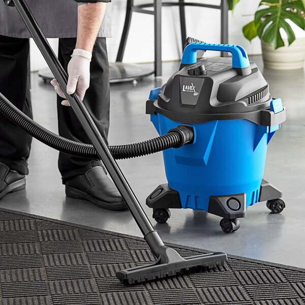 A person using a Lavex blue and black wet/dry vacuum to clean a carpet.