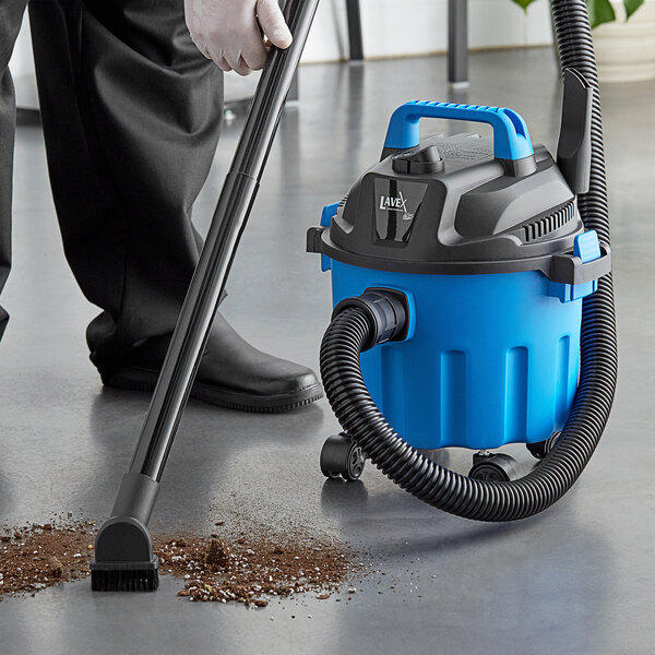 A person using a blue and black Lavex wet / dry vacuum to clean dirt off the floor.