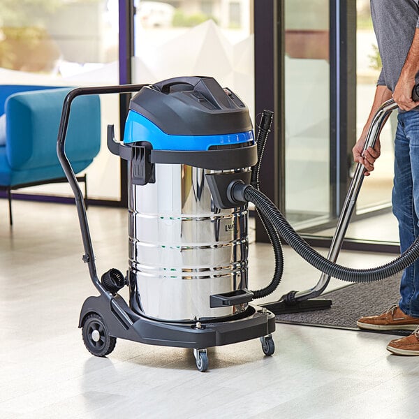 A man using a Lavex stainless steel wet/dry vacuum to clean a floor in a professional kitchen.