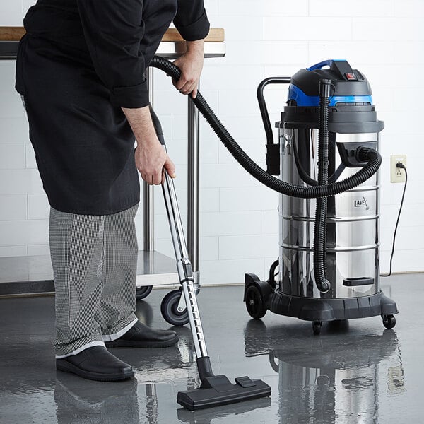A man using a Lavex stainless steel wet/dry vacuum in a professional kitchen.