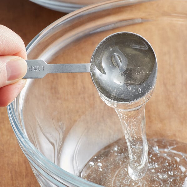 A hand using a spoon to pour Golden Barrel Corn Syrup into a bowl on a kitchen counter.