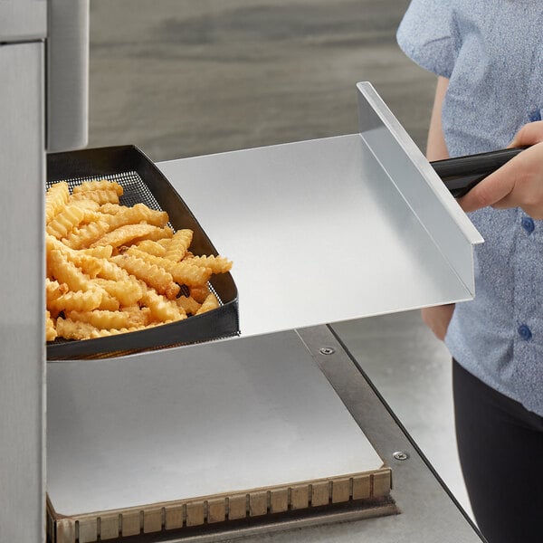 A person using a TurboChef paddle peel to remove fries from a high speed oven.