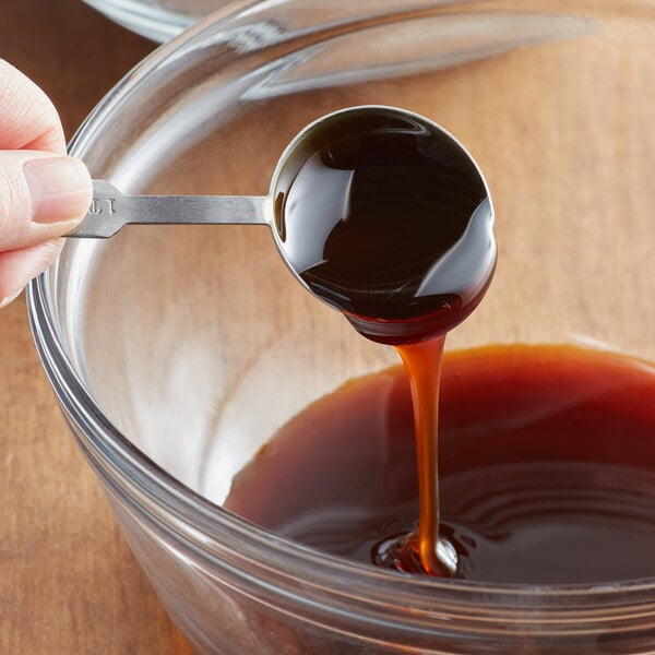 A spoon scoops liquid malt extract blend from a golden barrel.