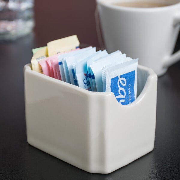 A white Hall China sugar packet holder on a counter with packets inside.