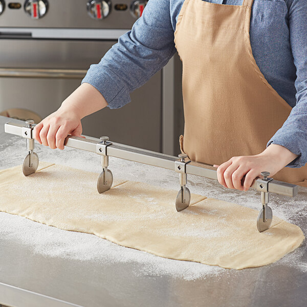 A person in an apron using an Ateco stainless steel multi-wheel pastry cutter to cut dough.