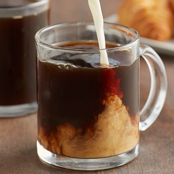 A glass mug filled with Caribou Coffee with a croissant on the side.