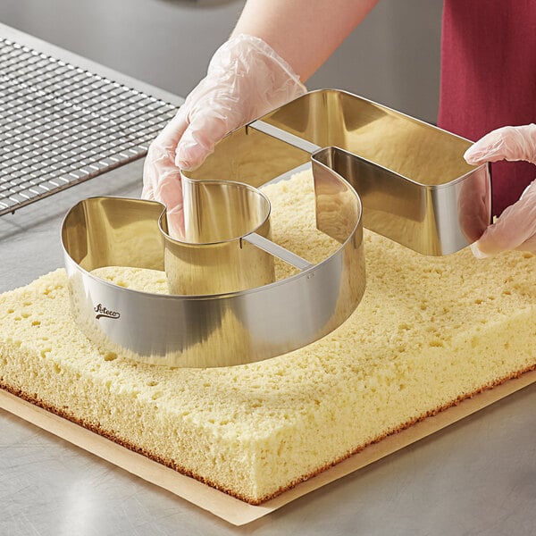 A person using a stainless steel Ateco number 5 cutter to cut a cake.