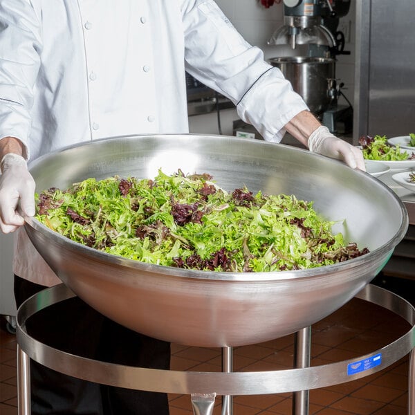 A chef holding a large Vollrath stainless steel mixing bowl filled with lettuce.