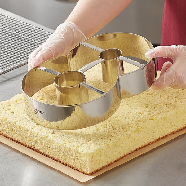 A person holding a metal Ateco number 8 cutter over a piece of cake.