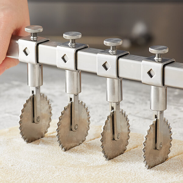 A hand holding an Ateco stainless steel fluted pastry cutter wheel over dough.