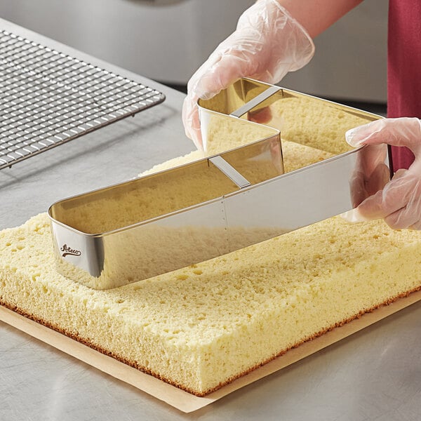 A person using an Ateco stainless steel number 7 cake cutter to cut a piece of cake.