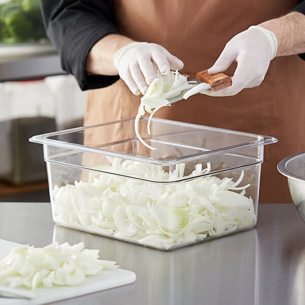 A person slicing onions in a Choice clear plastic food pan.