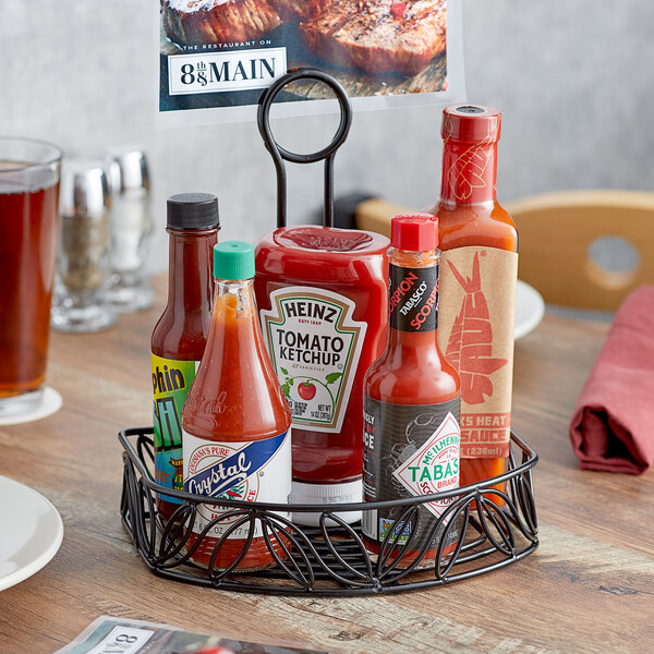 An American Metalcraft wrought iron condiment caddy on a table with bottles of hot sauce and mustard.