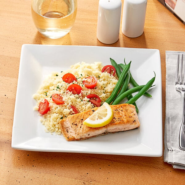 A Acopa Bright White square porcelain plate with salmon, rice, and vegetables on it with a lemon wedge.