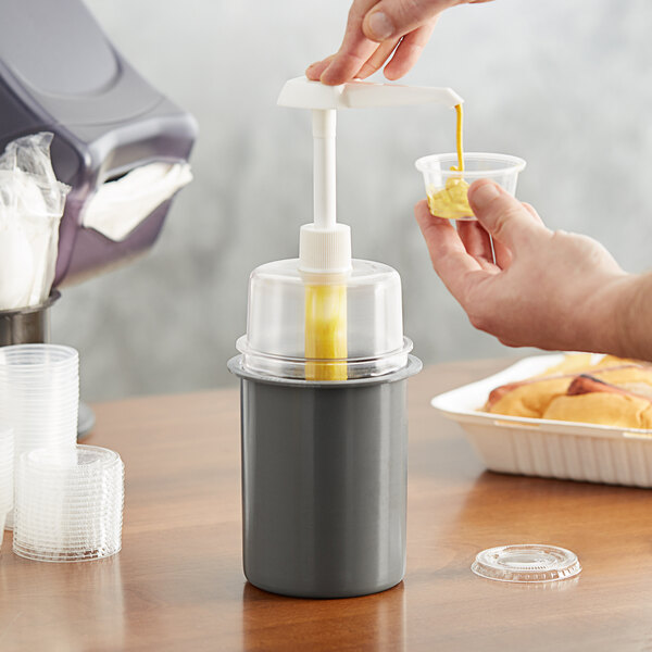 A person using a Steril-Sil condiment pump to pour mustard into a small container.