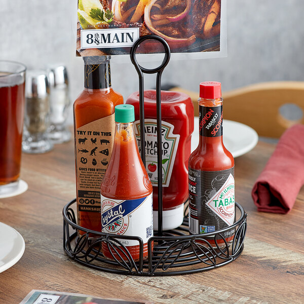 An American Metalcraft wrought iron condiment caddy holding hot sauces and ketchup on a table.