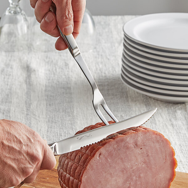 A person using a Vollrath carving knife and fork to cut ham.