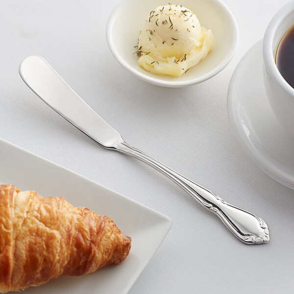 A plate with a croissant, butter, and an Acopa Blair stainless steel butter knife on it next to a cup of coffee.