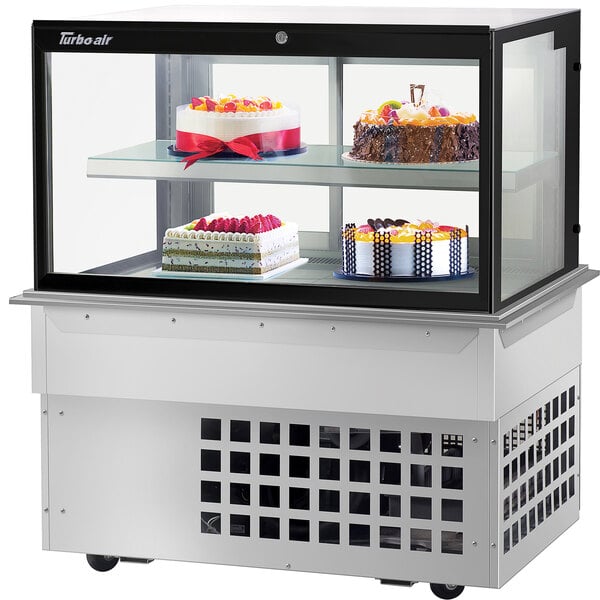 A Turbo-Air refrigerated bakery display case with cakes on two tiers of glass shelves.
