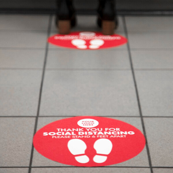 A red E-Z Up floor decal with white footprints that says "Social Distancing" in a circle.