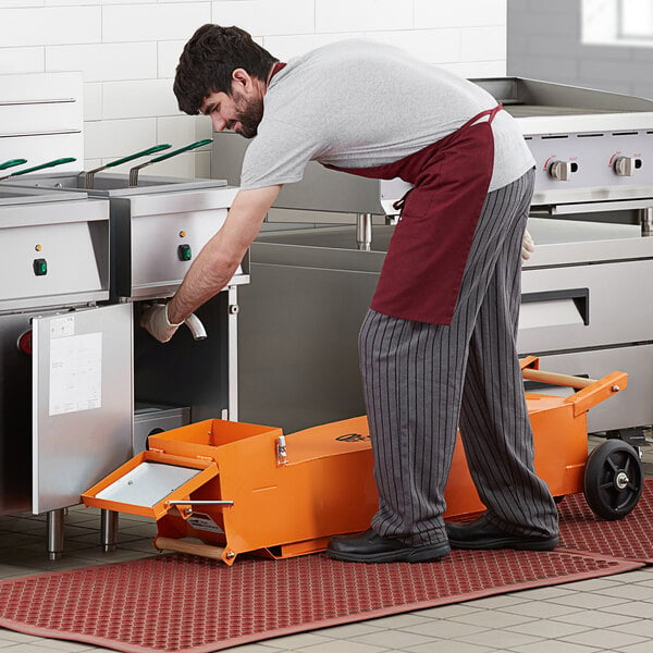 A man in a red apron uses a Fryclone fryer oil shuttle in a professional kitchen.