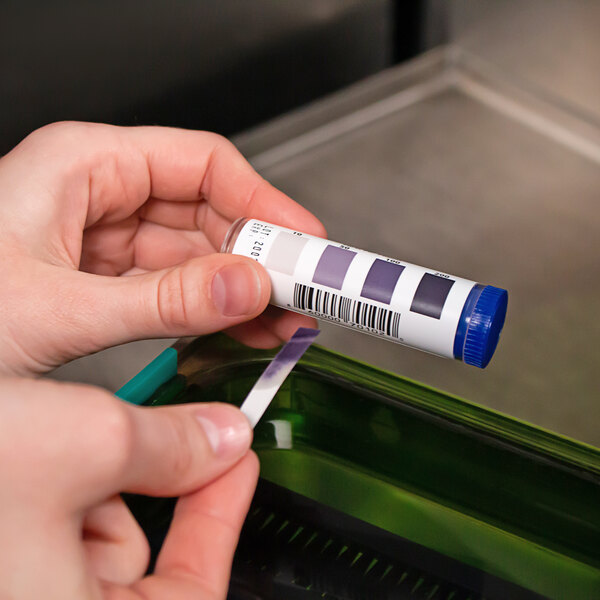A hand holding a test strip in a blue tube.