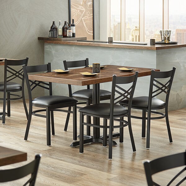 A Lancaster Table & Seating rectangular wood butcher block table with black chairs in a restaurant.