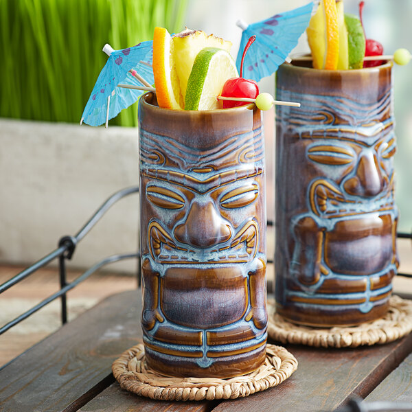 Two Tuxton ceramic tiki mugs filled with tropical fruit on a table.