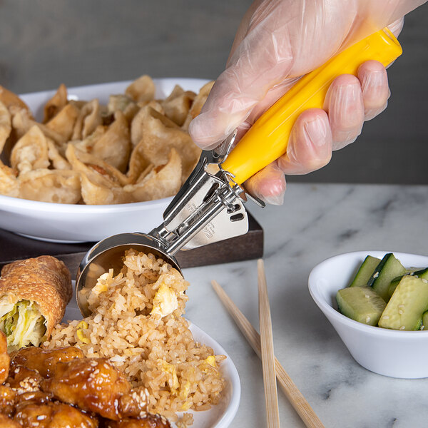 A hand using a Carlisle yellow thumb press disher to serve food.