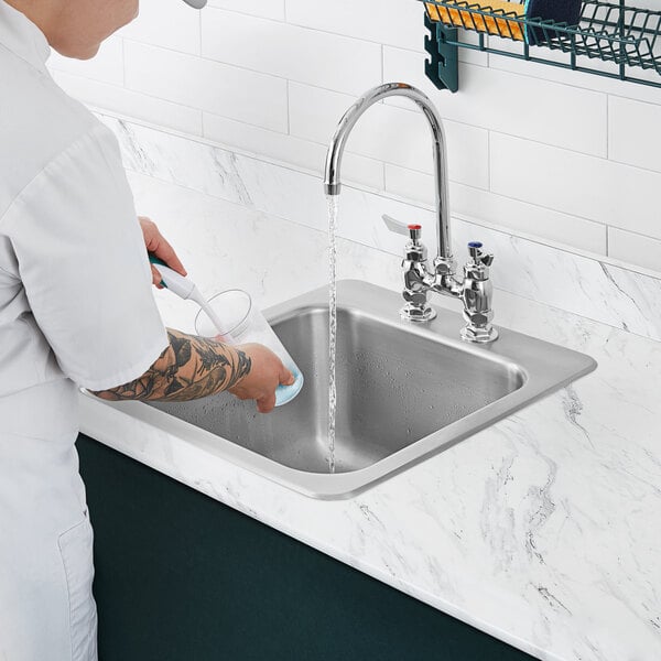 A person washing dishes in a Waterloo stainless steel drop-in sink.