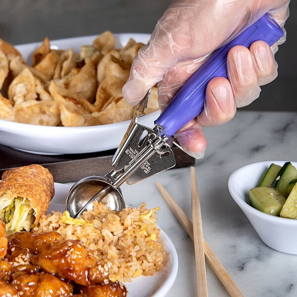 A person in a glove using a Carlisle purple thumb press scoop to serve food.